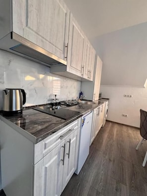 A kitchen with white cabinets, a black countertop, and a stainless steel kettle.