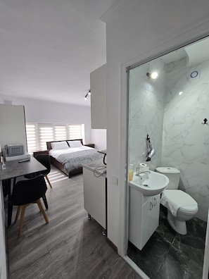 Ein modernes Hotelzimmer mit Bett, Schreibtisch, Stuhl und Badezimmer mit Toilette, Waschbecken und Spiegel.