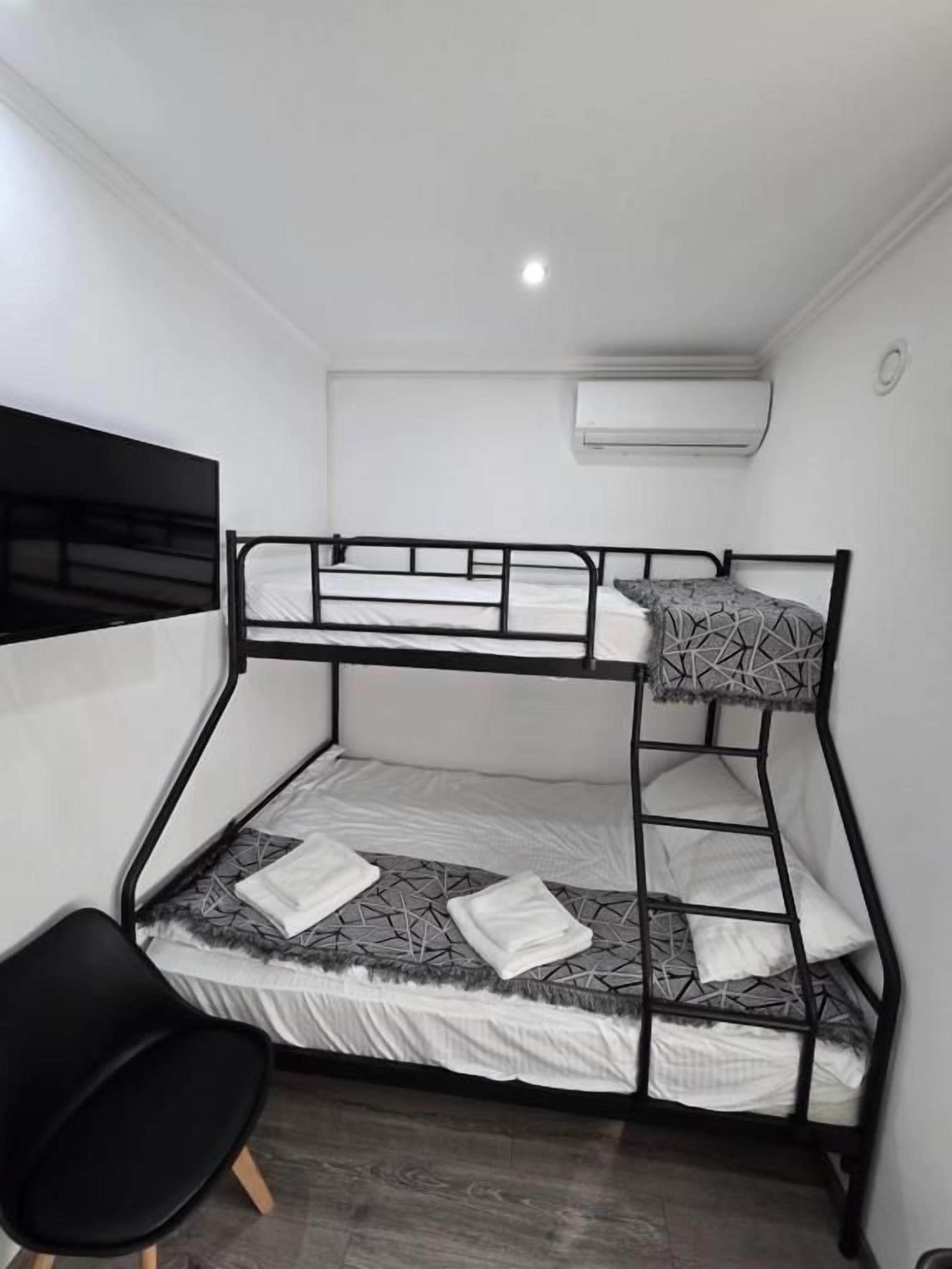 Una cama litera con escalera, una silla negra y un equipo de aire acondicionado en la pared.