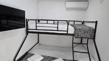 Una cama litera con escalera, una silla negra y un equipo de aire acondicionado en la pared.
