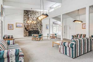 A spacious living room with a stone fireplace, striped sofas, and hanging pendant lights. - Charming, two-story ski condo w/ a wood stove, free WiFi, shared pool, & hot tub (Mammoth Lakes)
