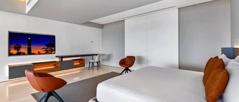 A modern hotel room with a large bed, a desk, two chairs, and a large window with a cityscape view.
