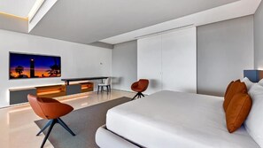 Una habitación de hotel moderna con una cama grande, un escritorio, dos sillas y un amplio ventanal con vista a la ciudad.