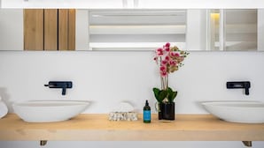Ein modernes Badezimmer mit zwei weißen Waschbecken, einem Spiegel und einer Topforchidee.