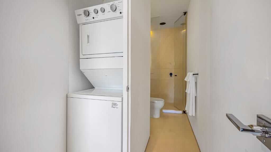 Un espace buanderie compact comprenant un lave-linge, un sèche-linge, des toilettes et une douche.