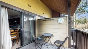 Un balcón con una mesa y sillas, un reloj y una puerta corrediza de vidrio que da a una cocina.