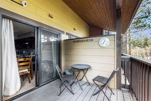 Ein Balkon mit Tisch und Stühlen, einer Uhr und einer Schiebetür zu einer Küche.