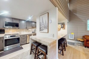 Eine moderne Küche mit einer zentralen Kochinsel, Edelstahlgeräten und einer Holzbeschichtung an der Decke.