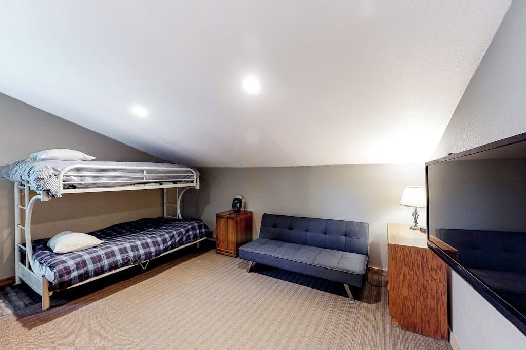 A room with a bunk bed, a sofa, a small wooden cabinet, and a television.