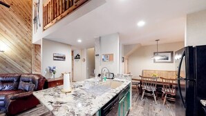 A kitchen with a marble countertop, wooden flooring, a dining area with wooden chairs, and a black refrigerator. - Renovated, Top-Floor Condo w/ Fireplace & Shared Hot Tub - Walk to Gondola (Mammoth Lakes)