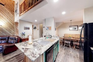 Eine Küche mit Marmorarbeitsplatte, Holzboden, einer Essecke mit Holzkästen und einem schwarzen Kühlschrank.