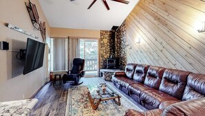 A living room with a leather sofa, a coffee table, a TV, a fireplace, and a ceiling fan. - Renovated, Top-Floor Condo w/ Fireplace & Shared Hot Tub - Walk to Gondola (Mammoth Lakes)
