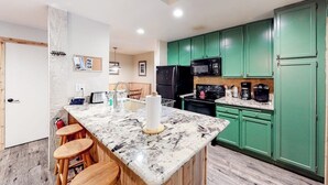 A kitchen with green cabinets, a marble countertop, and a black refrigerator. - Renovated, Top-Floor Condo w/ Fireplace & Shared Hot Tub - Walk to Gondola (Mammoth Lakes)