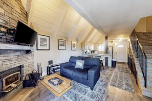 Ein Loft-Wohnbereich mit Kamin aus Stein, einer Couch, einem Couchtisch und einer Küche im Hintergrund.