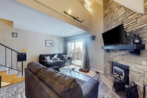 Ein Wohnzimmer mit Kamin aus Stein, einem Flachbildfernseher, einer Couch und einer Treppe.