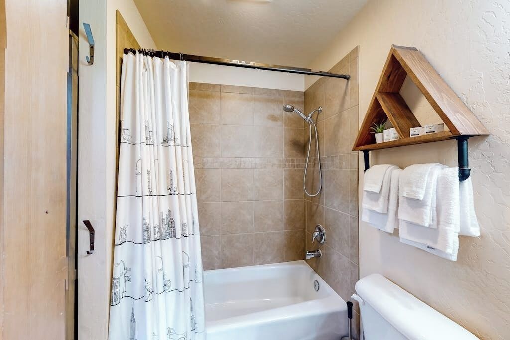 A bathroom with a bathtub, shower, and a shelf with towels.
