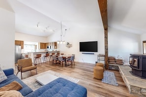 A modern living room with a sofa, a dining area with chairs, a kitchen in the background, and a fireplace. - Walk to Village & Gondola Corner Condo w/ Fireplace, WiFi & Shared Hot Tub (Mammoth Lakes)
