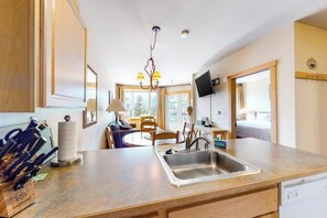 A kitchen with a sink, a dining area with chairs, a chandelier, and a television mounted on the wall. - Beautiful & Convenient Suite Close to Activities w/Shared Pool & Hot Tub, WiFi (Mammoth Lakes)