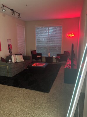 A living room with a sofa, chairs, a coffee table, a TV, and a red neon sign. - Cozy 1-bedroom apartment with AC in charming midtown Houston (Houston)