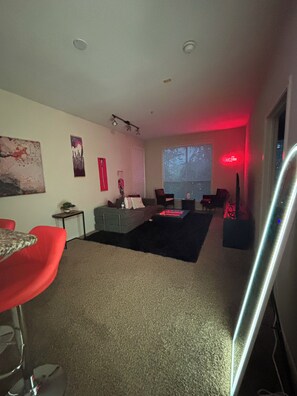 A modern living room with a sofa, a coffee table, and a dining area with red chairs. - Cozy 1-bedroom apartment with AC in charming midtown Houston (Houston)