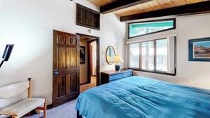 Um quarto com uma cama grande, um banco de madeira, uma porta, uma janela e um abajur.