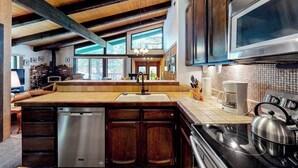 Cozinha com vigas de madeira, uma ilha grande, eletrodomésticos de aço inoxidável e vista para o exterior.