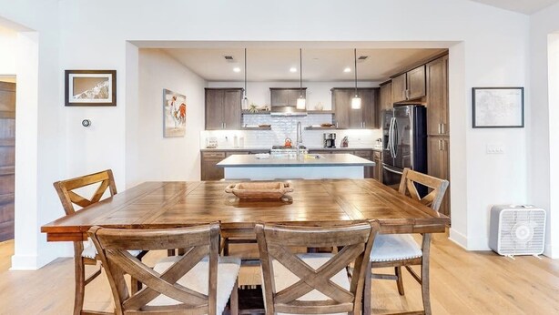 A modern kitchen with wooden cabinets, a central island, pendant lighting, and a dining area with a wooden table and chairs. - Luxe, Modern Townhome w/ Mountain Views & WiFi - Close to Golf & Skiing (Mammoth Lakes)