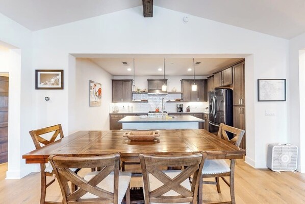 A modern kitchen with wooden cabinets, a central island, pendant lighting, and a dining area with a wooden table and chairs. - Luxe, Modern Townhome w/ Mountain Views & WiFi - Close to Golf & Skiing (Mammoth Lakes)