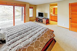 A bedroom with a large bed, a television, a wooden cabinet, and a bathroom visible through an open door. - Mountain View Condo in Old Mammoth w/ Balcony, Fireplace & 3 Shared Hot Tubs (Mammoth Lakes)