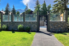 A gated entrance with a stone wall, a metal gate, and a paved path leading to a building. - Mountain View Condo in Old Mammoth w/ Balcony, Fireplace & 3 Shared Hot Tubs (Mammoth Lakes)