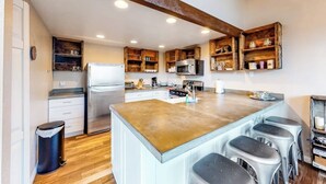 Una cucina con isola centrale, sgabelli da bar, mobili in legno e frigorifero in acciaio inossidabile.