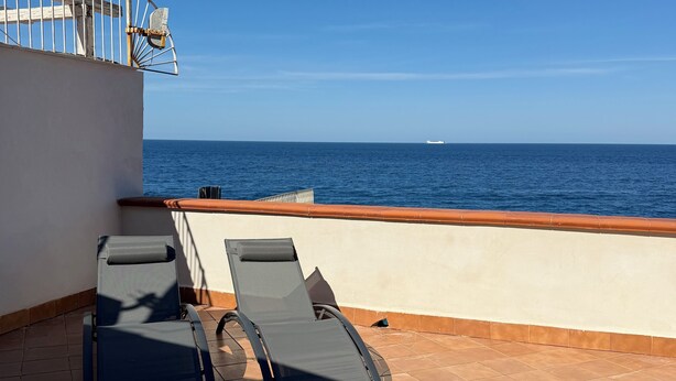 Eine Terrasse mit zwei Liegestühlen, einem Geländer und Blick aufs Meer.