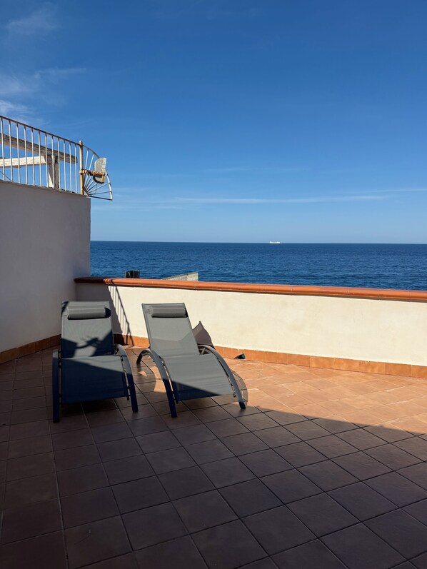 Eine Terrasse mit zwei Liegestühlen, einem Geländer und Blick aufs Meer.