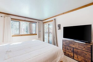 A bedroom with a bed, a TV on a wooden dresser, and large windows. - Home with Views, Shared Pool & Hot Tub - Near the Slopes (Mammoth Lakes)