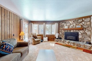 A cozy living room with a stone fireplace, wooden walls, and a comfortable seating area. - Home with Views, Shared Pool & Hot Tub - Near the Slopes (Mammoth Lakes)