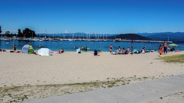 Una spiaggia con tende, persone e barche in acqua.