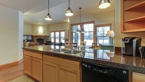 Una cucina con piani di lavoro in granito, mobili in legno, lavastoviglie e illuminazione a sospensione.