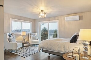 Ein Schlafzimmer mit einem großen Bett, zwei Stühlen, einem kleinen Tisch, einer Lampe und Blick ins Freie.