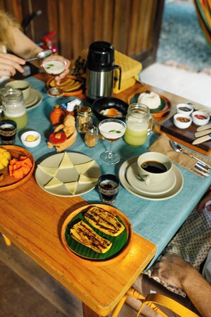 Una mesa de madera con varios platos, incluyendo una fuente de fruta cortada, una taza de café y un vaso de una bebida verde.