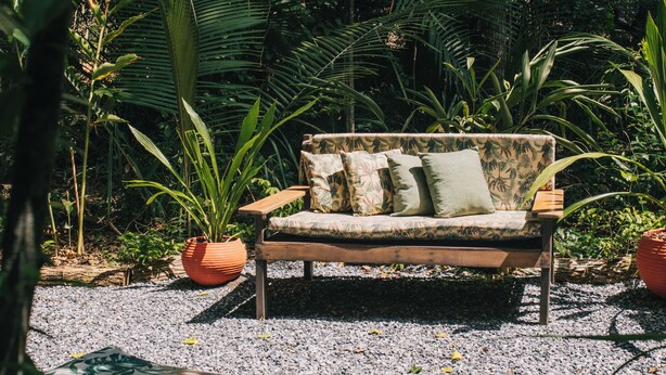 Un jardín con un banco de madera, un sofá y plantas en macetas.