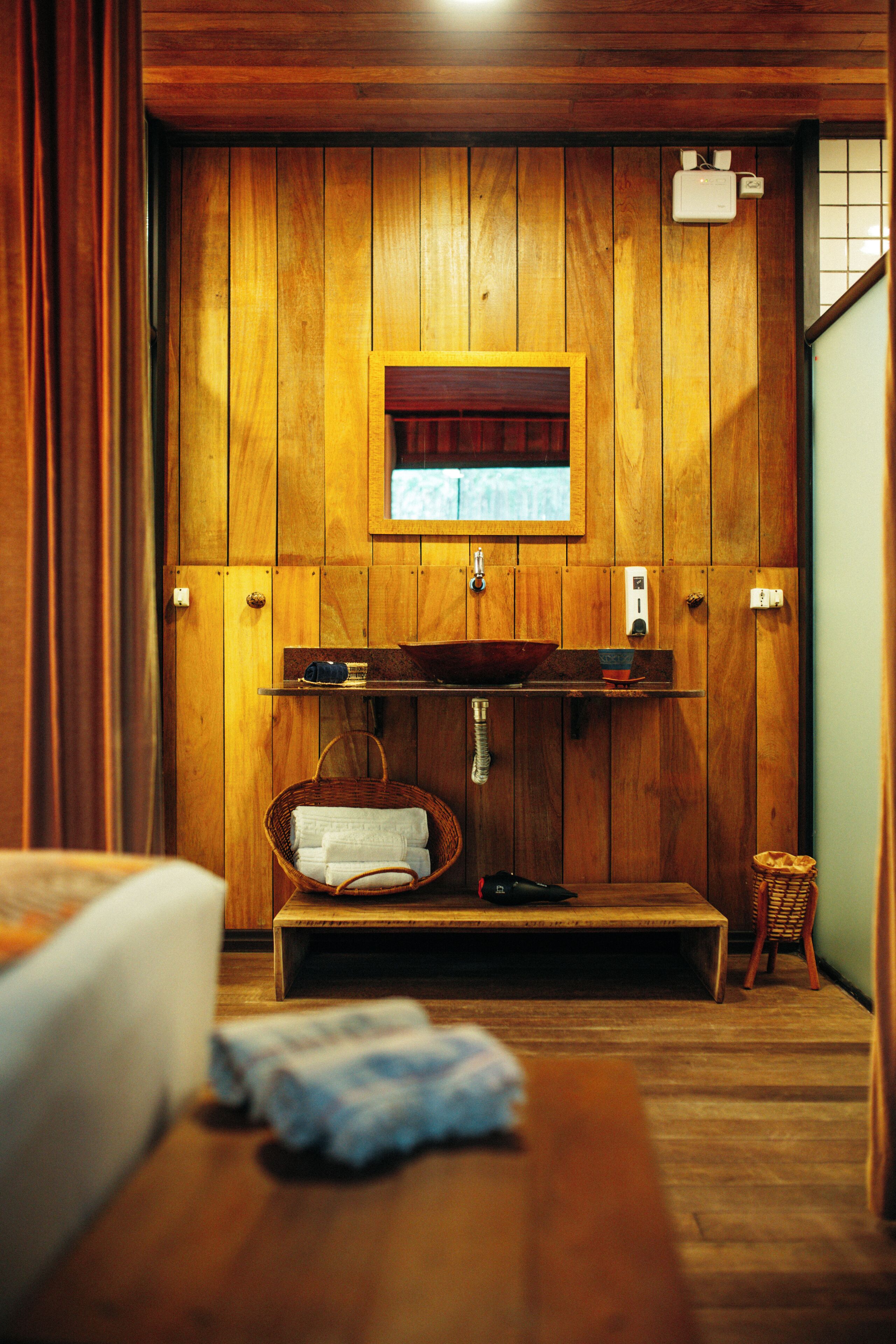 Quarto de madeira com um banco de madeira, uma pia pequena e uma janela.