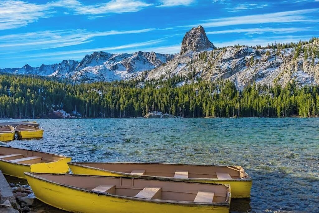 A clear lake with boats, a mountain, and a forest.