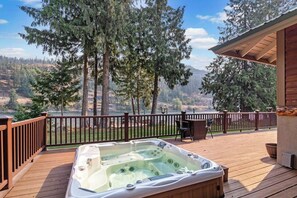 A hot tub on a wooden deck with a view of a forest and hills.