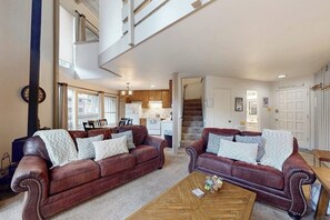 A spacious living room with two leather sofas, a coffee table, and a staircase leading to an upper floor. - Perfect Condo W/ Shared Pools/Hot Tubs, Free WiFi, Full Kitchen & Balcony (Mammoth Lakes)
