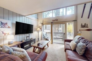 A living room with a TV, wooden coffee table, leather sofa, and a large window. - Perfect Condo W/ Shared Pools/Hot Tubs, Free WiFi, Full Kitchen & Balcony (Mammoth Lakes)