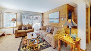 A living room with two sofas, a coffee table, a rug, and a wooden desk with a lamp. - Inviting condo 500 feet to canyon lodge lifts w/on-site pool, hot tub, sauna (Mammoth Lakes)