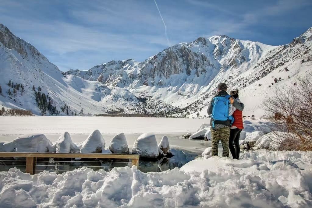 A snowy mountainous landscape with a frozen lake and a wooden dock.