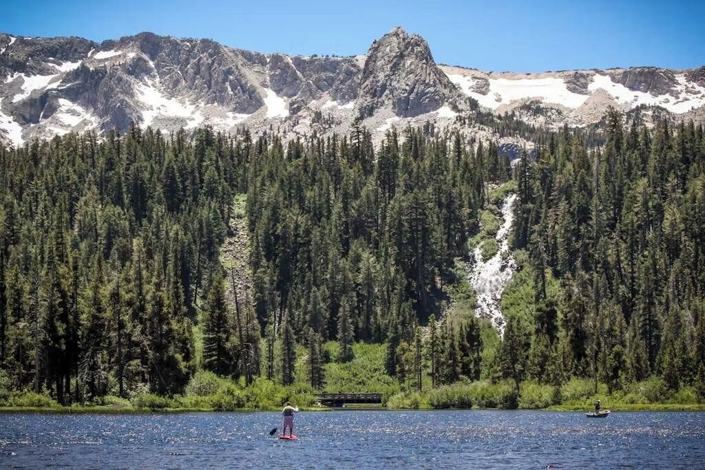 A lake with a mountain backdrop, a person paddleboarding, and a small boat.