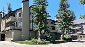 A multi-story building with a central entrance, balconies, and a landscaped area with trees. - Inviting condo 500 feet to canyon lodge lifts w/on-site pool, hot tub, sauna (Mammoth Lakes)