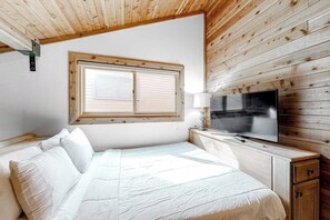 A bedroom with a bed, a television, a window, and wooden walls. - Spacious condo near skiing with fireplace, washer/dryer, deck & full kitchen (Mammoth Lakes)